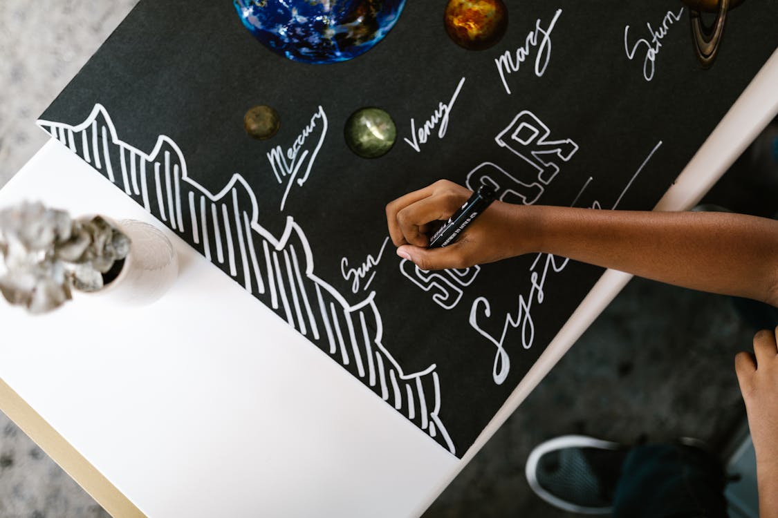 A child writing on a poster with a black marker, representing the creation of visual aids
