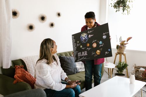 Free A boy presents a homemade solar system project to his mother in a cozy living room. Stock Photo