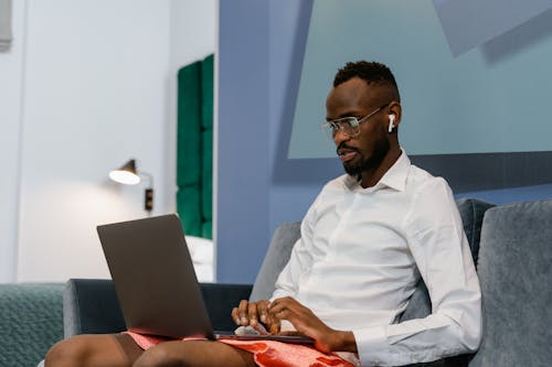 A Man in White Long Sleeve Shirt Sitting on Sofa While Using a Laptop