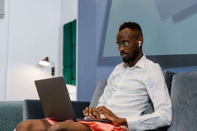 A Man In White Long Sleeve Shirt Sitting On Sofa While Using A Laptop