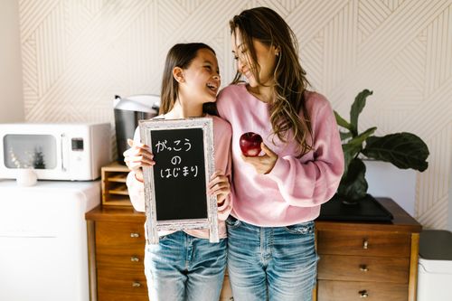 Free Mother and daughter smiling with a back-to-school chalkboard, creating a joyful family moment. Stock Photo