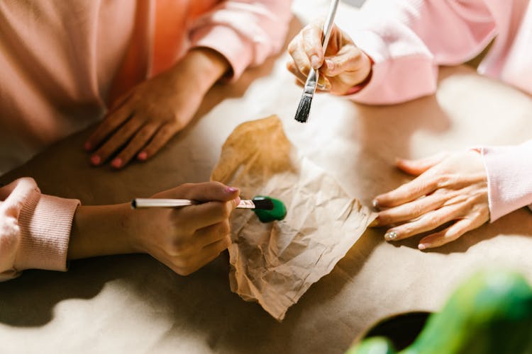 Girls Putting Paintbrush Into Green Paint