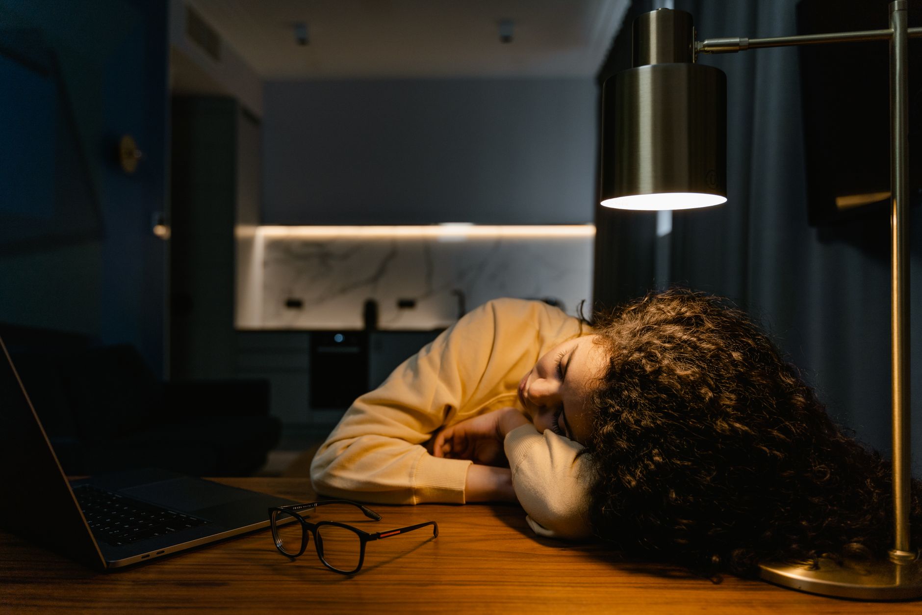A woman asleep at her desk beside a laptop, illustrating the rise in sedentary time that accompanied restricted sleep in the trial.