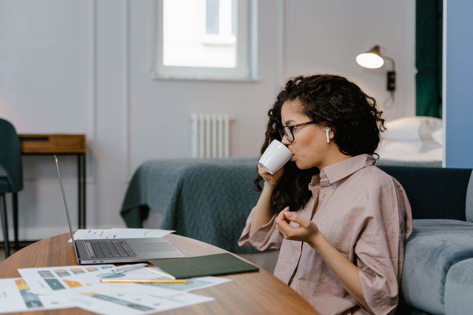 Woman enjoying coffee while telecommuting from home office with laptop.
