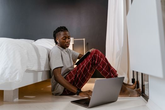 A young adult using a laptop and tablet while sitting on the floor, symbolizing remote work lifestyle.