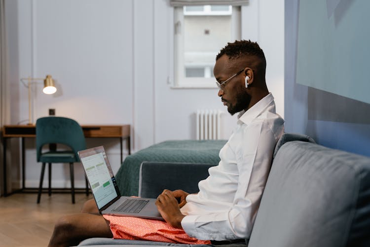 A Man In A Dress Shirt Working On His Laptop While Sitting On The Couch At Home