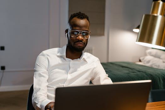 An adult man focused on remote work using a laptop in a stylish bedroom office.