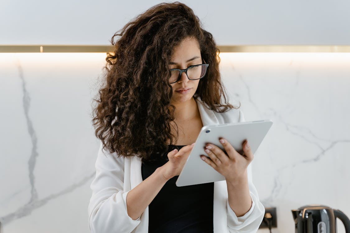 Free A woman uses a tablet in a modern kitchen, focusing on technology and multitasking. Stock Photo