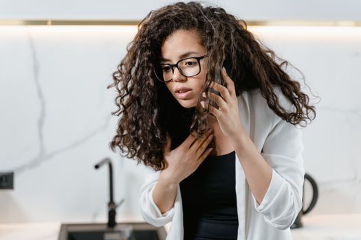 Young woman with curly hair making an urgent phone call indoors, looking concerned.