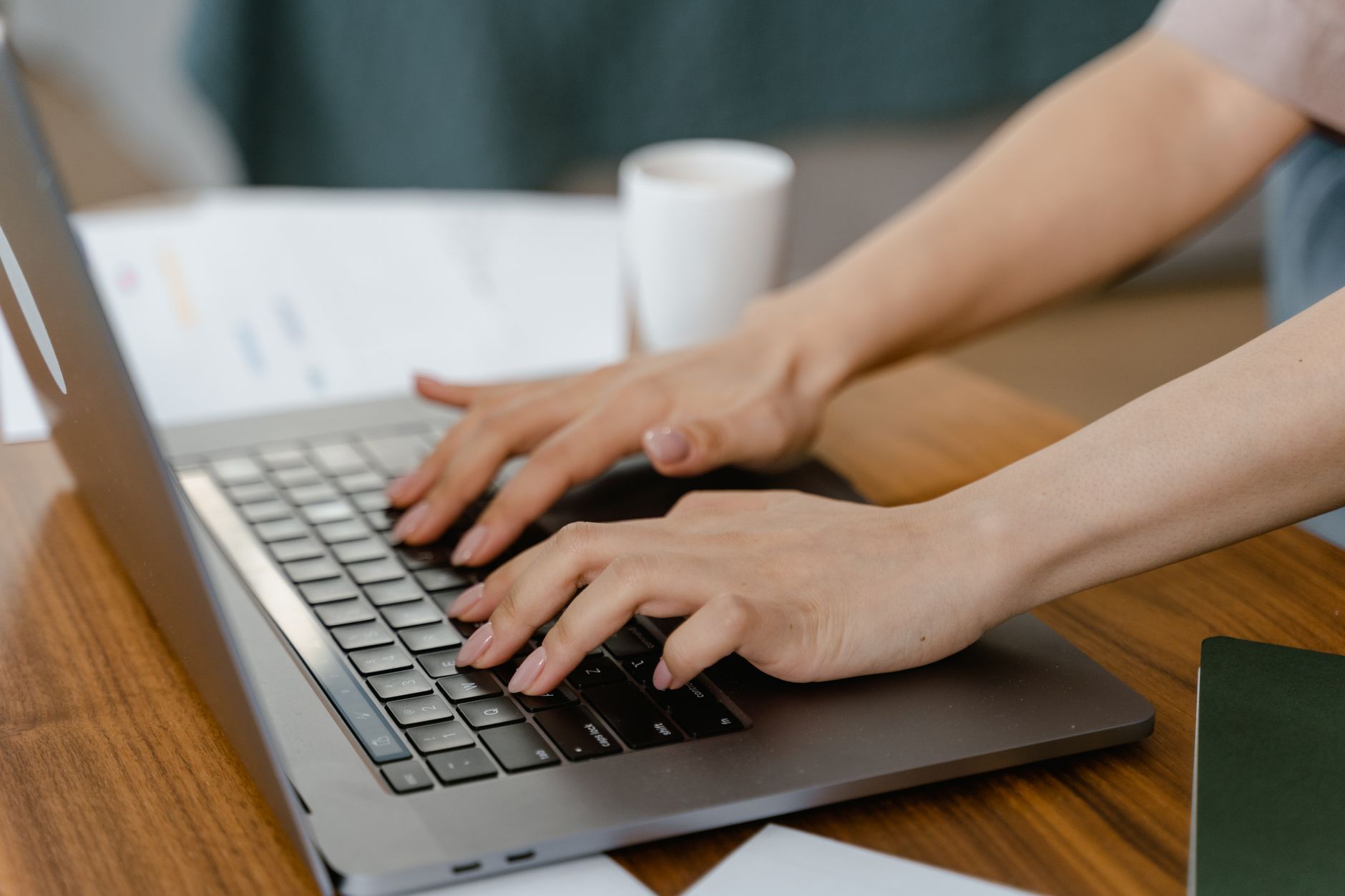 Primer plano de una mujer escribiendo en un portátil en un ambiente interior acogedor, enfocándose en la productividad.