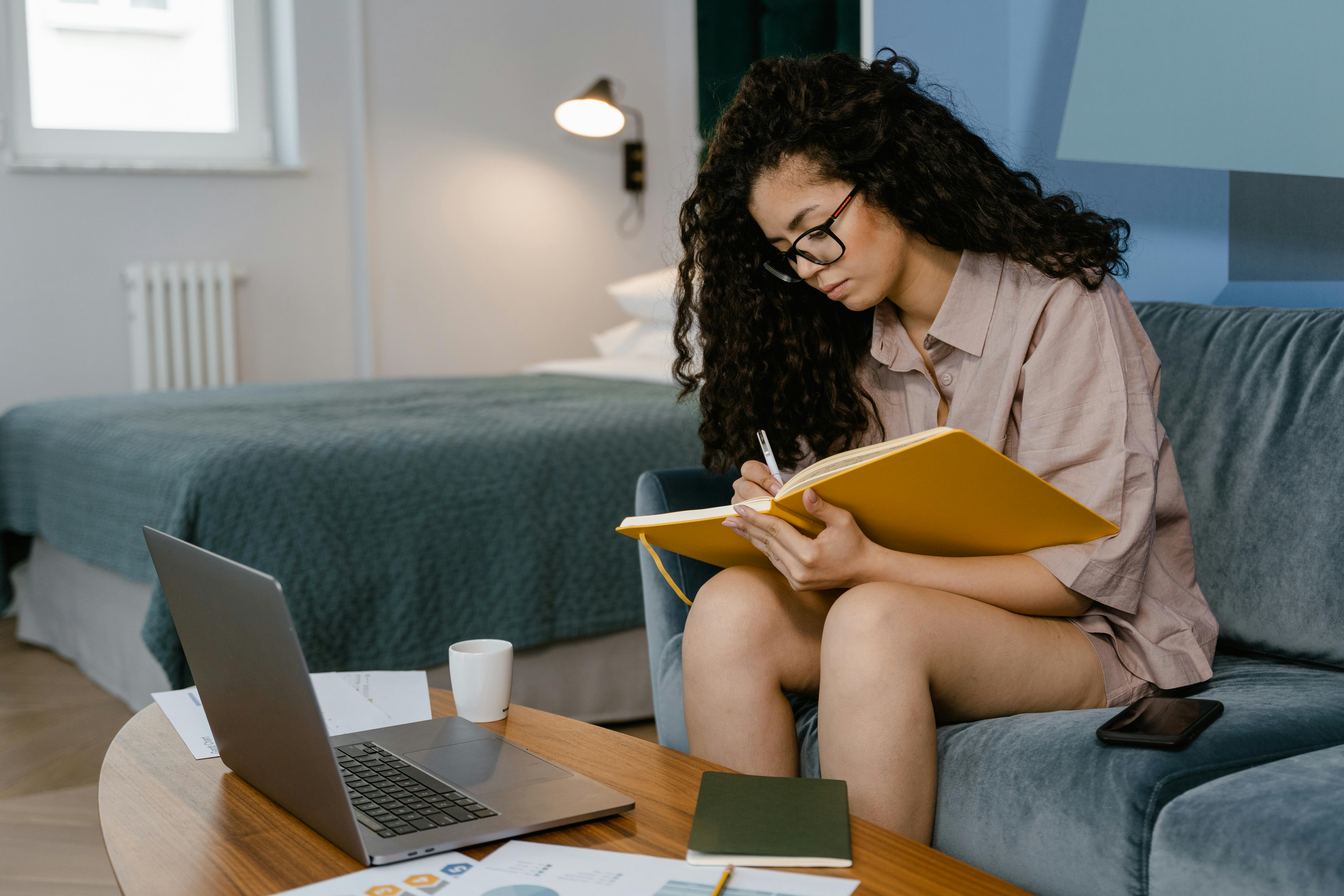 a young woman writing in a notebook while sitting on a couch