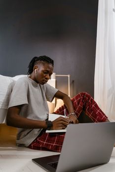 Focused young adult working on a laptop at home, wearing casual pajamas, illustrating remote work lifestyle.