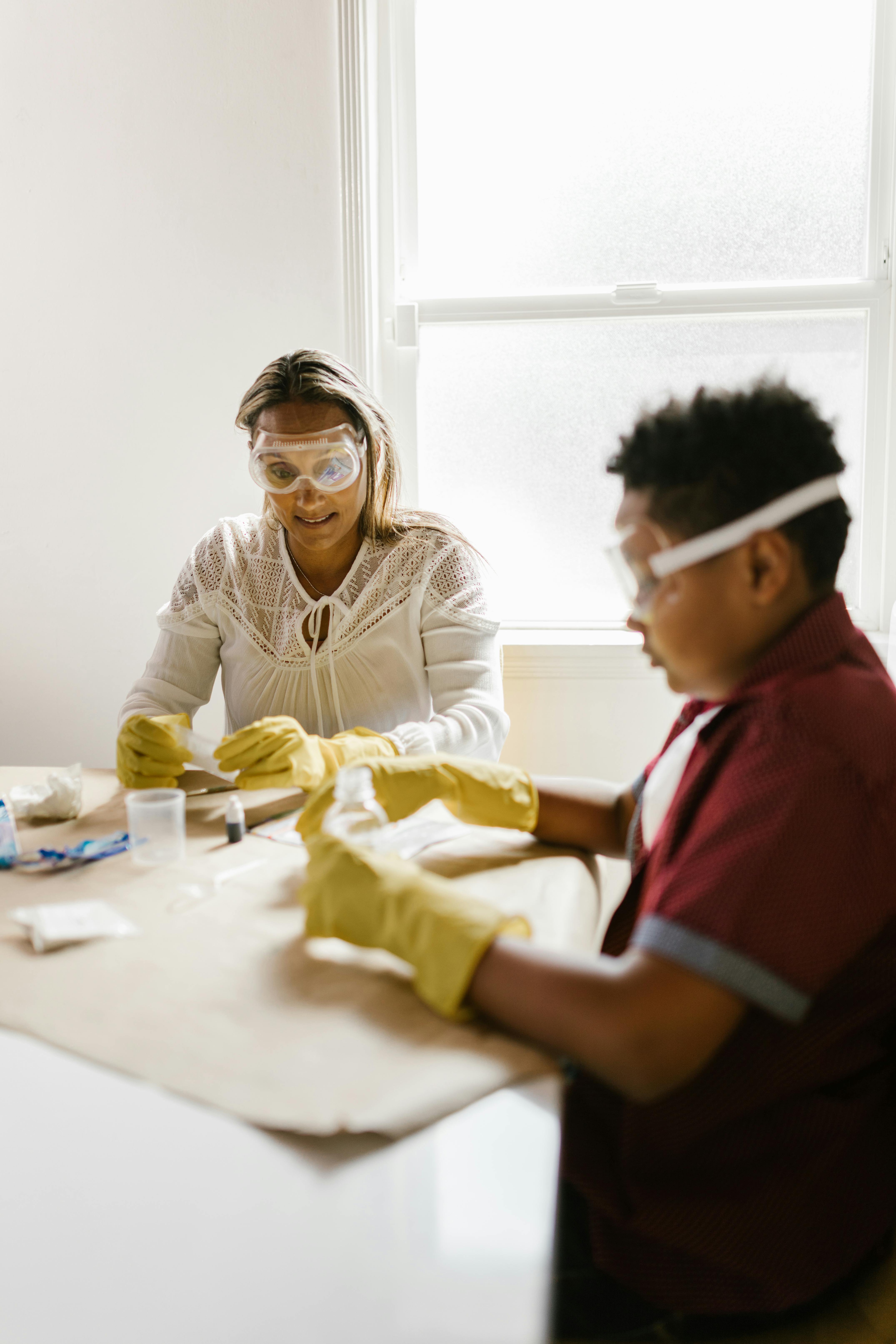 a woman and a boy wearing gloves and protective goggles while working at the table