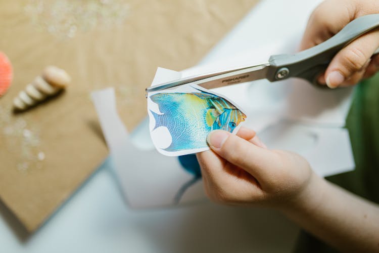 A Person Cutting A Printed Fish In A Paper