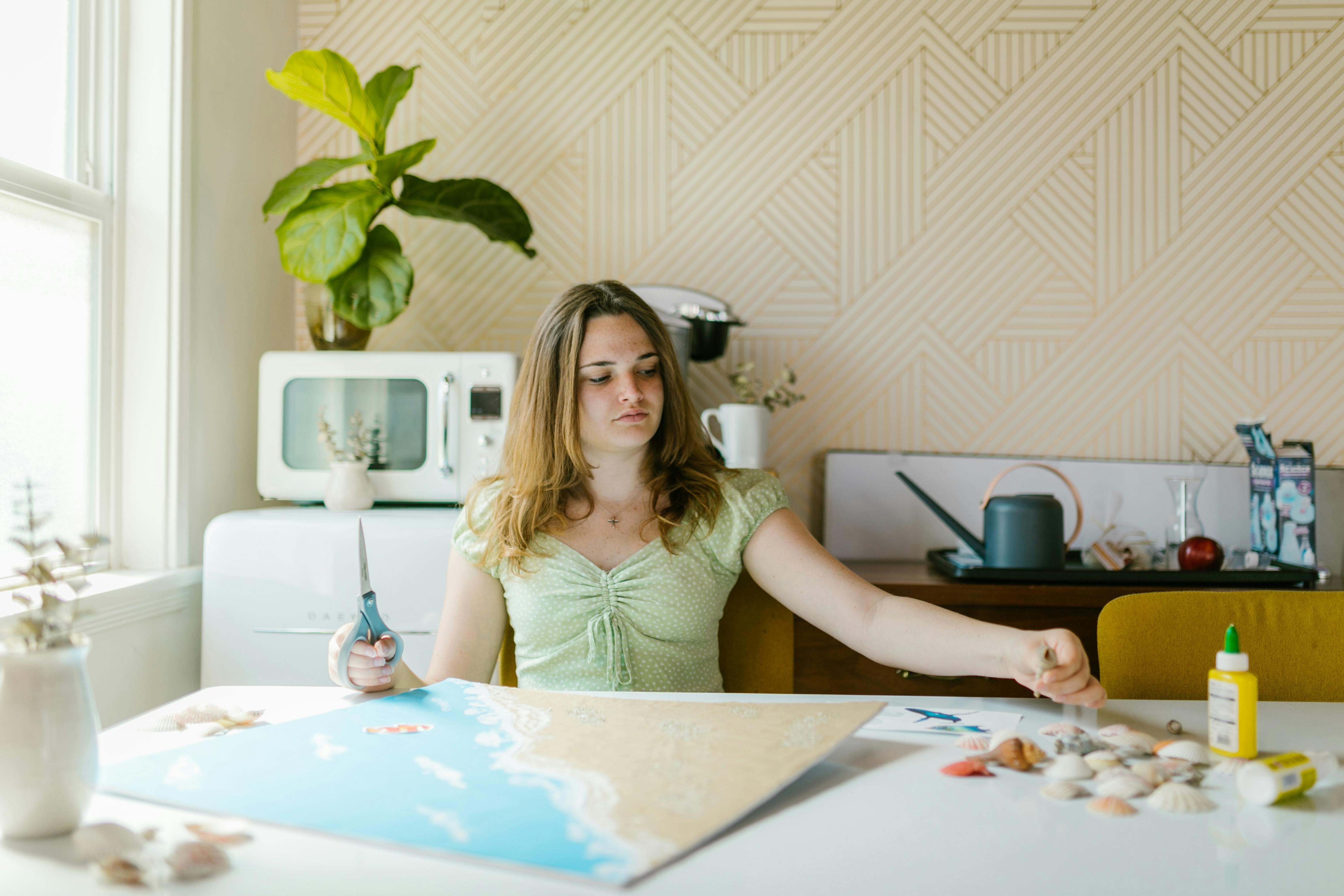 A young woman creating an arts and crafts project indoors with scissors and glue.