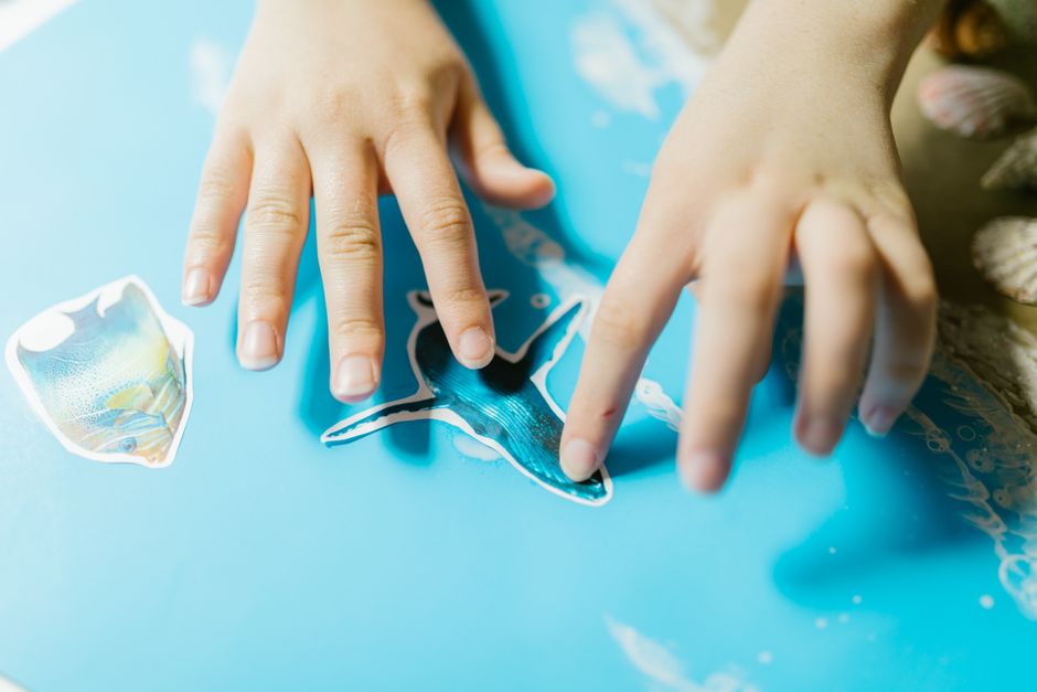 子供がクラフト活動中に青い紙と魚の切り抜きを使ってアートを作成しています。