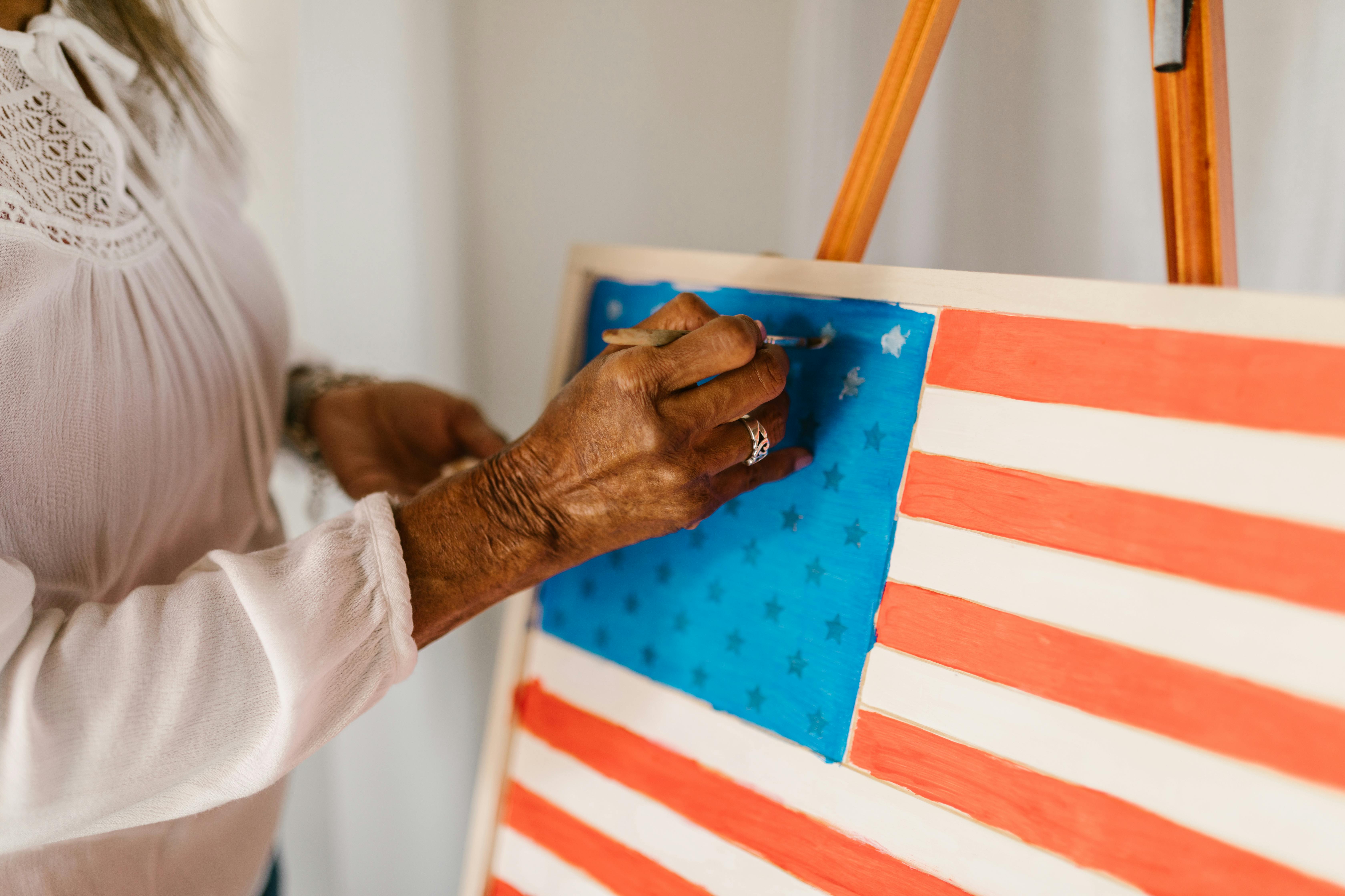 Artist painting the American flag on canvas in a bright studio.