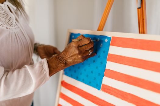 Artist painting the American flag on canvas in a bright studio.