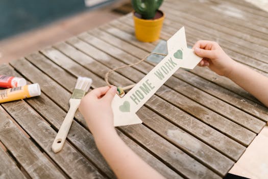Hands creating a homework sign on a rustic wooden table with paints and brushes.
