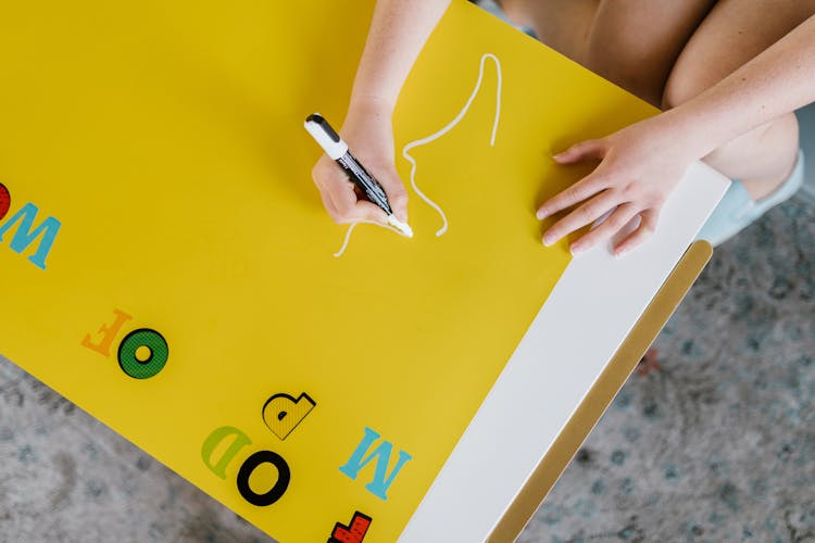 Hands Of A Person Holding A White Pen Drawing On A Yellow Paper