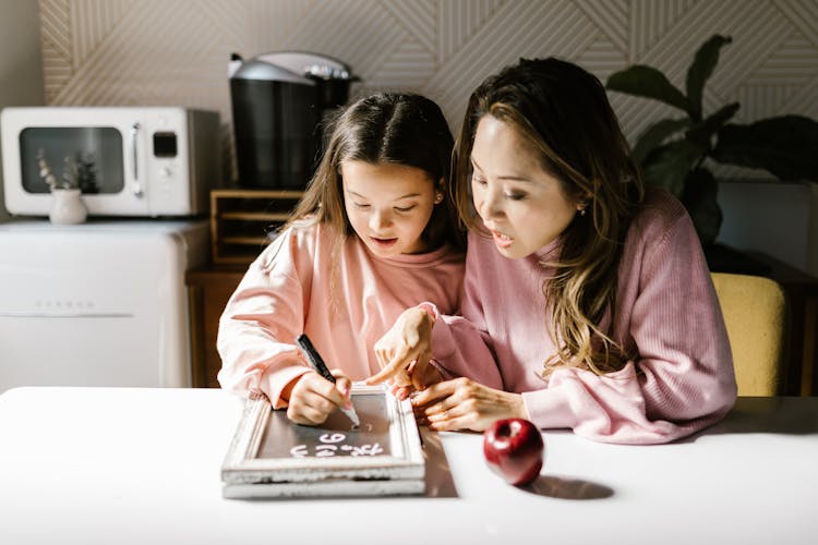 Woman In Pink Long Sleeves And A Girl Writing On A Board