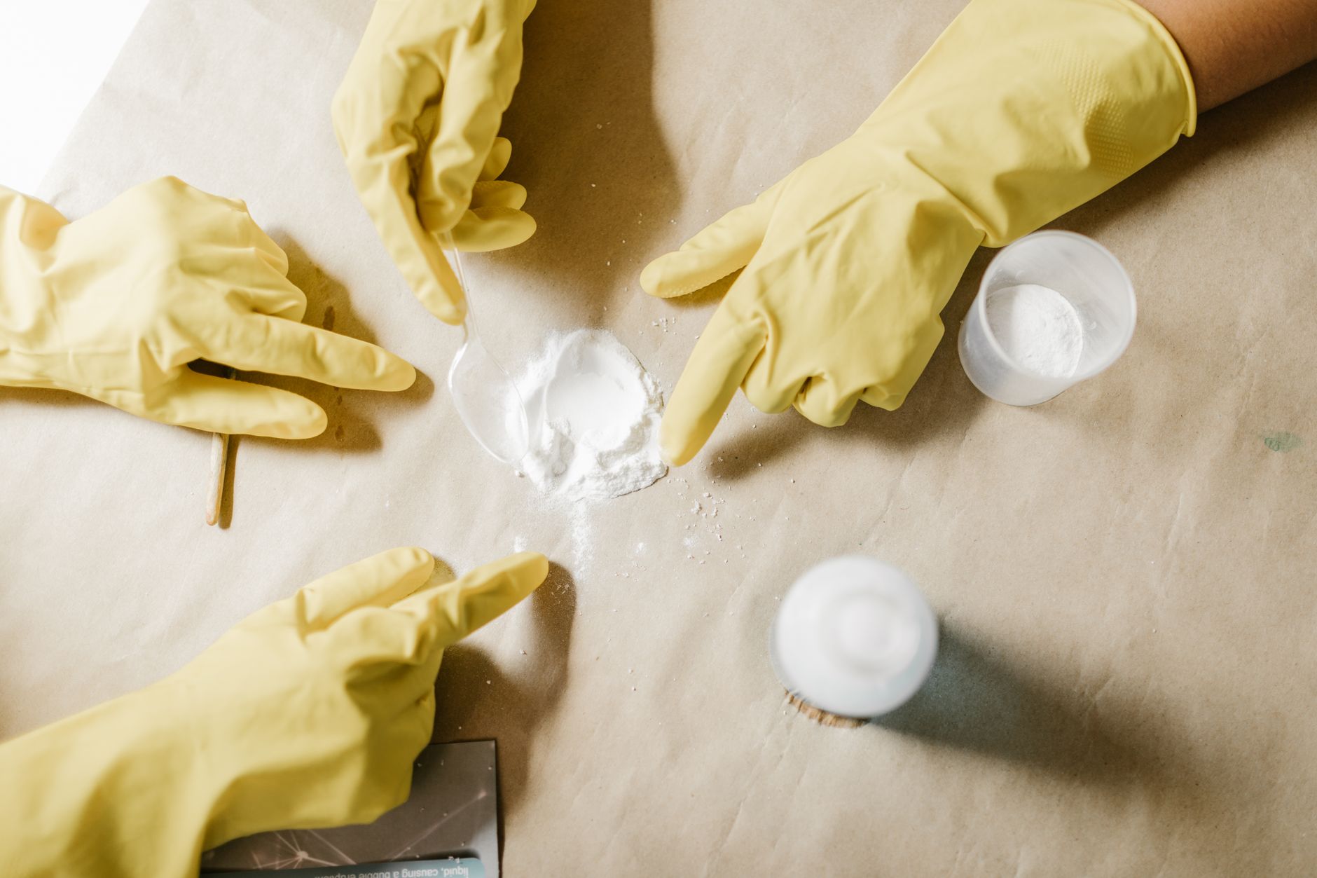 A top view of hands in latex gloves conducting a powder experiment on brown paper.