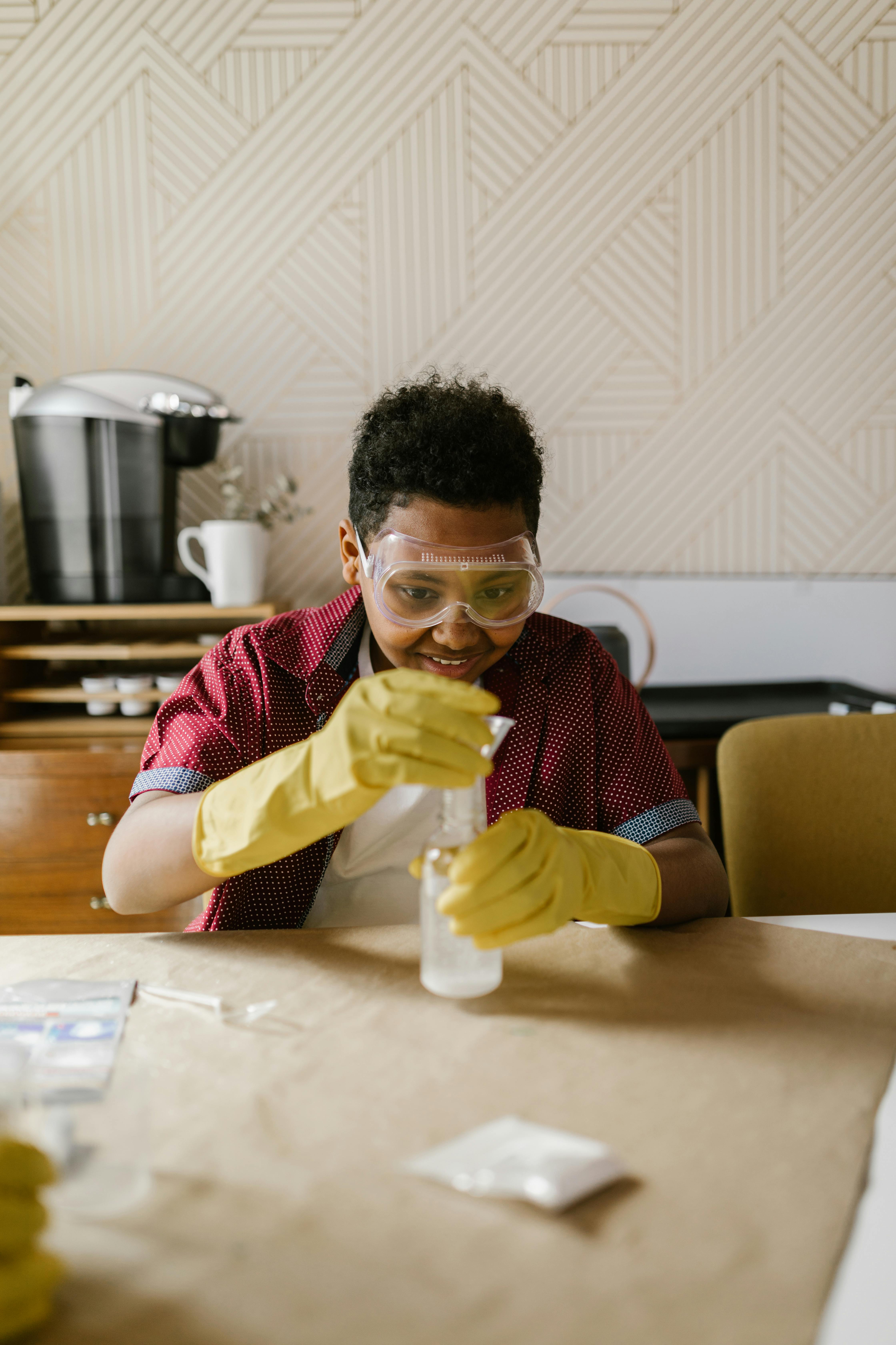 A child conducting a science experiment with concentration, wearing protective gear indoors.