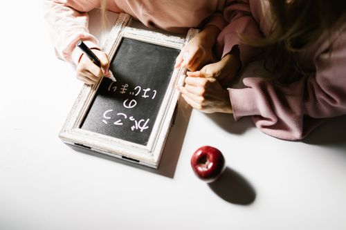 Free Two children writing on a blackboard, with a red apple resting on the table. Stock Photo