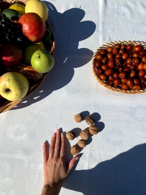 A vibrant display of apples, walnuts, and fruits on a white linen tablecloth with a person's hand.