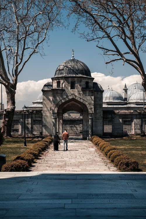 Free A couple walks towards a historic mosque entrance under a clear blue sky. Stock Photo