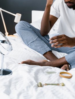 A man sitting on a bed using a jade roller for self-care, promoting relaxation.