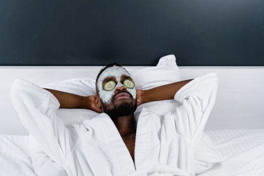 An adult man in a bathrobe relaxing with a cucumber face mask, exemplifying self-care and relaxation.