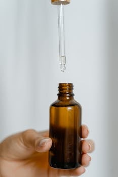 A hand holding a brown glass bottle with a dropper against a white background.