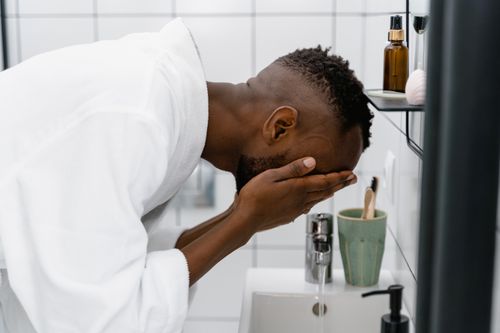 Free A man in a white robe washing his face at a bathroom sink, focusing on self-care and hygiene. Stock Photo