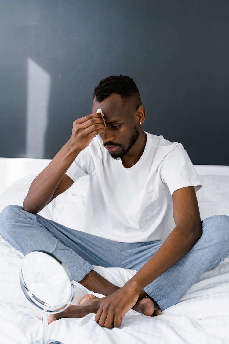 Man In White Crew Neck T-shirt And Blue Pants Sitting On White Bed