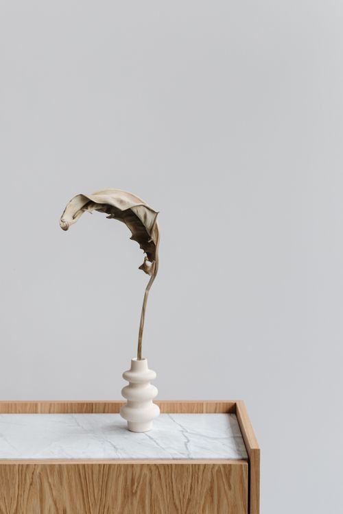 Free Simple minimalist decor featuring a dried leaf in an artistic vase on a wooden surface. Stock Photo