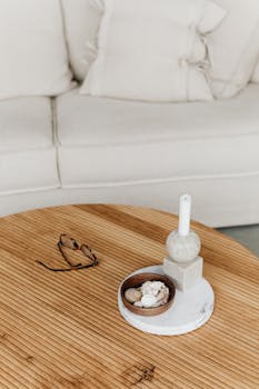 Minimalist living room featuring a wooden coffee table with a candle, eyeglasses, and decorative items.