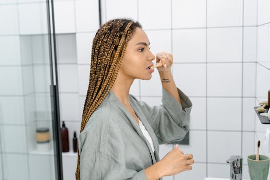 Woman with braided hair brushing teeth in a modern bathroom, promoting self-care.