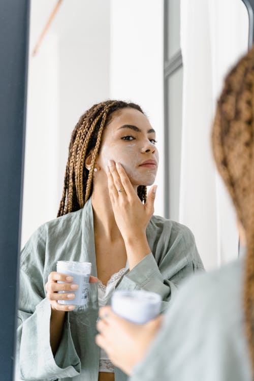 Free A Woman Looking at the Mirror while Applying a Cream on Her Face Stock Photo