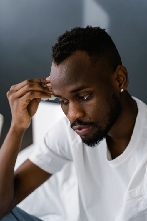 Free A pensive young man in a white shirt sits indoors, deep in thought. Stock Photo
