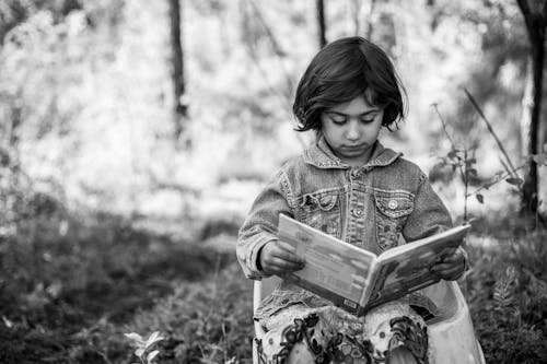 A Grayscale Photo of a Young Girl Reading a Book