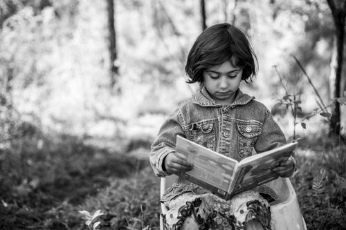 Free Black and white photo of a young girl reading outside in nature. Stock Photo