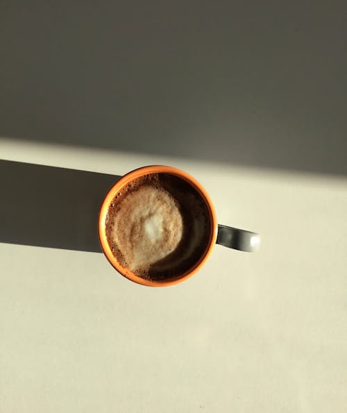 Free Top view of aromatic hot frothy cappuccino in ceramic mug placed on table in sunlight Stock Photo