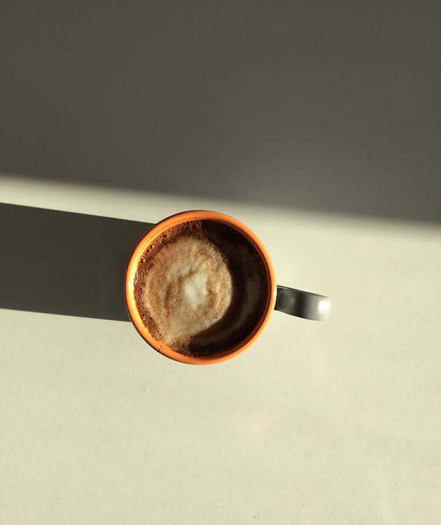 Top view of aromatic hot frothy cappuccino in ceramic mug placed on table in sunlight