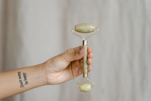 A person holds a jade roller, a skincare tool, in their hand. Neutral background enhances focus.