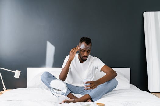 Man applying facial cream in a bedroom for skincare routine indoors.