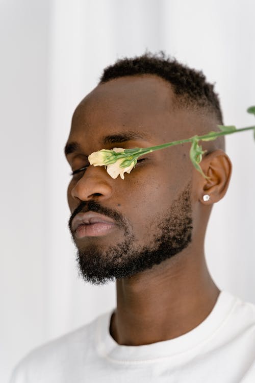 A Man in White Shirt Covering His One Eye with a Flower