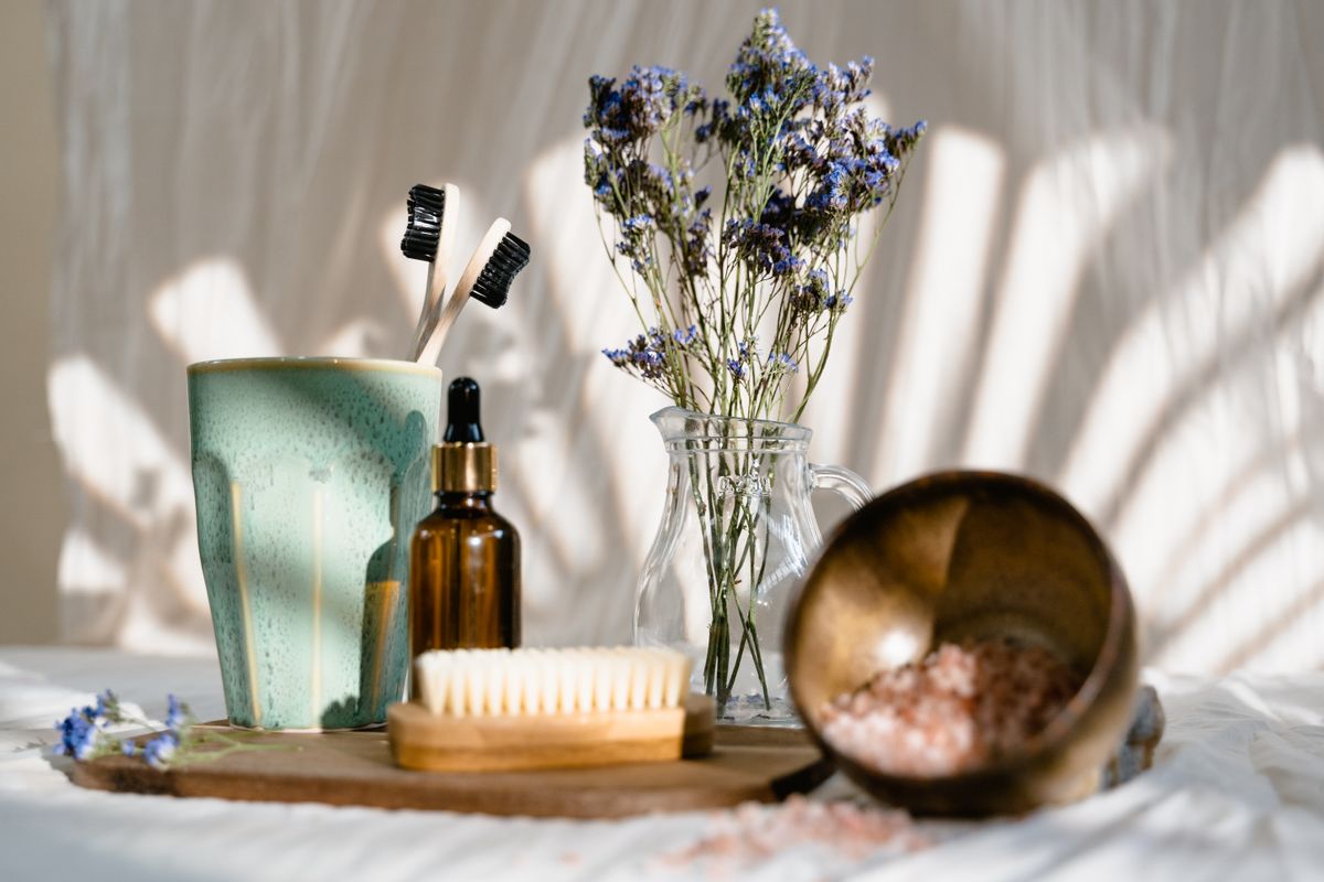 Skincare bottle, brush and pink salt arranged on white linen