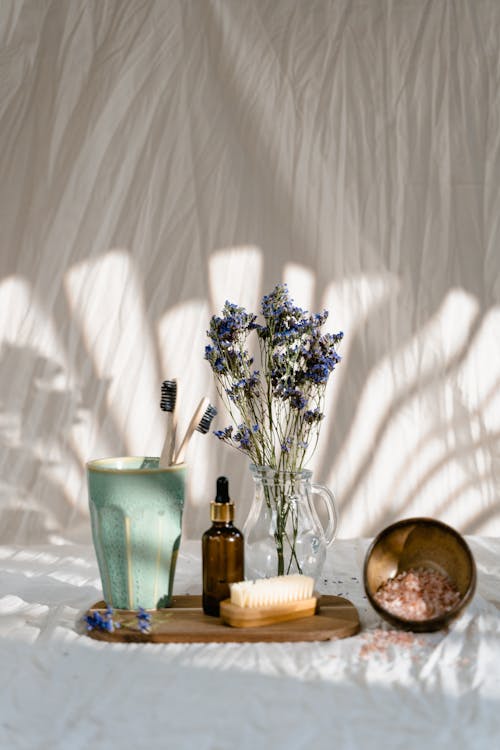 An image of a glass bottle, flowers on a vase, and a ceramic cup on a wooden tray