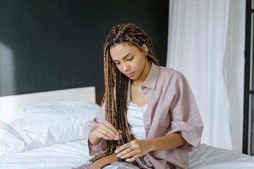 Free A Woman Sitting on Her Bed while Holding a Glass Bottle Stock Photo